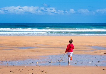 boy in red sweatshirt running on the beach with a stick in his hand