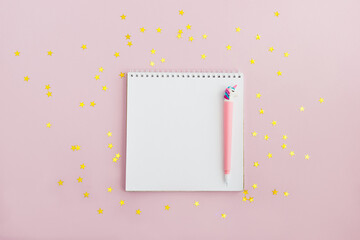Notebook and unicorn pen on a pink background with golden star confetti. Setting goals for the year. The concept of making wishes. Copy space, layout, top view.
