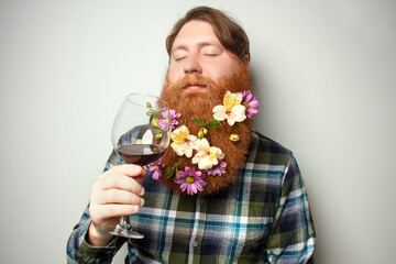 A red-bearded man with a decorated beard for the holiday drinking wine from a large glass. A vine tasting at home. Sommelier for yourself at home. A man with a big beautiful beard.