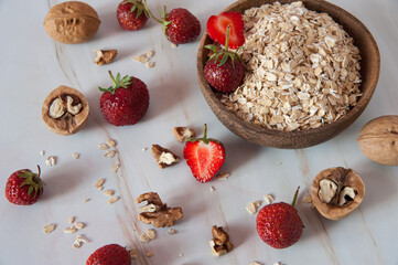 Home cooking. Healthy Breakfast of oatmeal, walnuts and fresh delicious organic strawberries close-up on a light marble background. Selective focus.