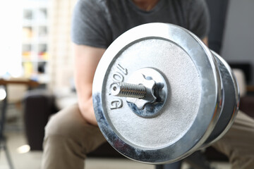 Close-up of male person lifting heavy metal dumbbell sitting on chair. Strong fit body. Training...