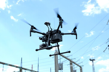 Pro quadcopter with camera aboard flying in a sky, electric pylon, cables and insulators on the background