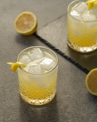Alcoholic drink gin tonic cocktail with lemon and ice on black stone table. Iced drink with gin.