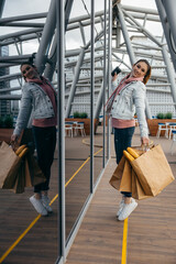 Smiling young woman holding coffee cup, walking with grocery shopping paper bag with long white...