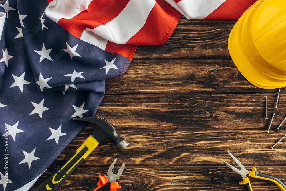 Sticker top view of american flag and instruments near safety helmet on wooden surface, labor day concept