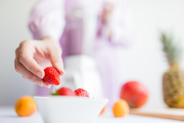 Close up of female picking up strawberry to make fruit shake in blender. Healthy vegetarian meal preparation.