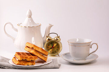 Belgian waffles in powdered sugar with bananas on a white plate. In the background, a teapot and a Cup for morning tea. Delicious breakfast.