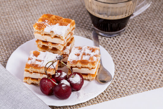 Belgian waffles in powdered sugar with bananas and cherries on a white plate.