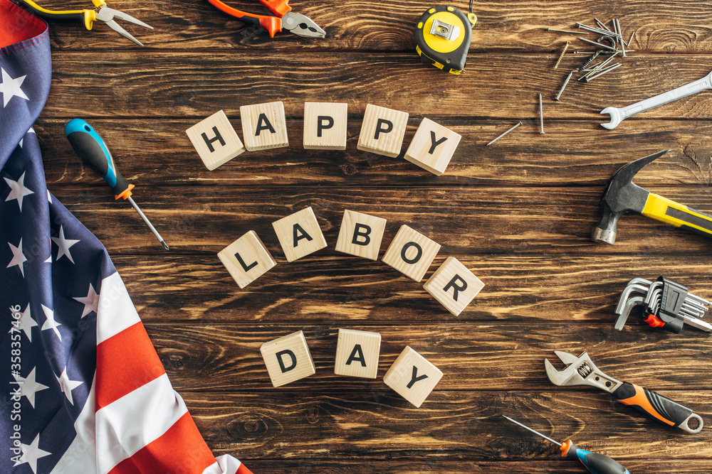 Sticker top view of tools and american flag near cubes with happy labor day lettering on wooden surface