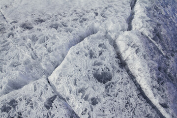 Naklejka premium Danger on the show surface: cracks in blue ice of cracked glacier in textured white snow surface under sunlight, closeup view, winter