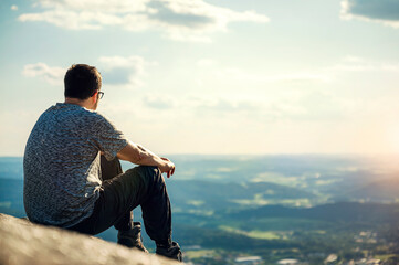 A young man sits on a rock at sunset and enjoys the view. Copy space