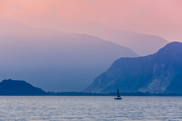 Pink dawn on lake Maggiore, Italy. A small sailing yacht against the background of the Alpine mountains and the dawn sky. Fog over the mountains.
