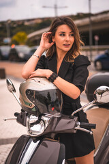 Fototapeta na wymiar Lifestyle session on a motorcycle, a young blonde Caucasian businesswoman with a black blazer and white pants. Sitting on the bike resting on the helmet