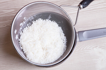 Freshly cooked rice in a strainer on a wooden background