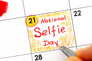 Woman fingers with pen writing reminder National Selfie Day in calendar.