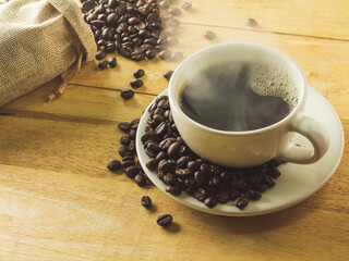 Roasted coffee beans with a cup of smoke on a wooden background.