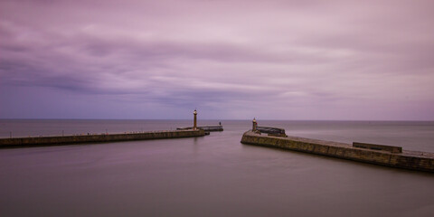 Long exposure of Whitby harbour showing the piers and lighthouses. UK coastline at dusk