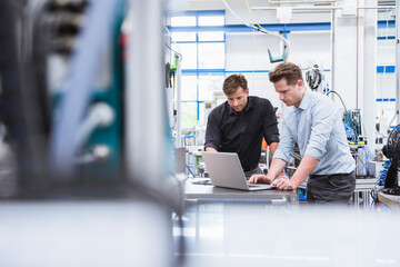 Two men using laptop in factory