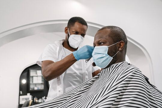Barber wearing surgical mask and gloves cutting hair of customer