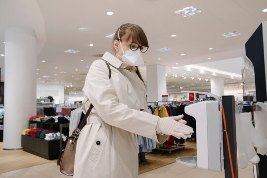 Woman With Face Mask And Disposable Gloves Disinfecting Her Hands Before Shopping In A Fashion Store