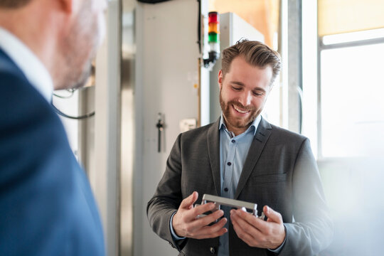 Smiling young businessman in a factory holding workpiece