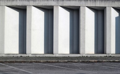 White concrete wall with long vertical shadows in the indentations. Sidewalk and asphalt street in...