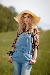 girl with curly hair and in denim overalls stands in nature

