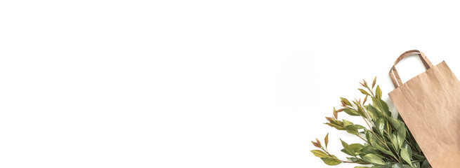 Recycled brown paper shopping bag with handle and green branches leaves isolated on white background. Zero waste concept. Top view, flat lay, copy space. Banner.