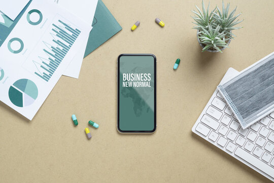 Business New Normal After Covid 19 Outbreak Background Concept. Mockup Mobile Phone For Covid19 Business New Normal With Facial Mask, Medicine Tablet, Financial Chart On Working Table.