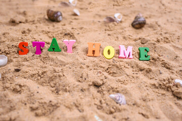 Fototapeta na wymiar Beach sand, shells, summer, and words in wood letters stay at home.