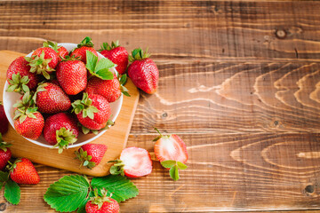 Ripe sweet strawberries in white plate on the wooden background. Copy space