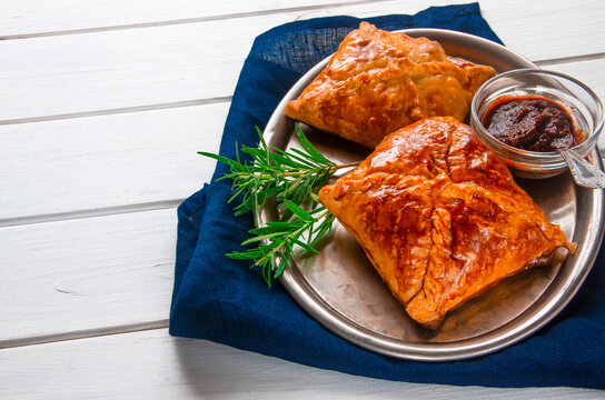 Homemade pastries with meat and spicy sauce with rosemary served on a metal tray on white wooden table