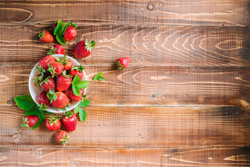 Ripe sweet strawberries in white plate on the wooden background. Copy space