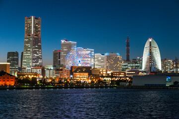 Fototapeta premium The skyline of the Minato Mirai district in Yokohama lights up at sunset.