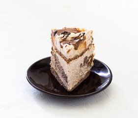 A piece of sponge cake with cream, caramel, nuts and chocolate on a light background