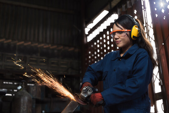 Young female engineer operating manufacturing equipment with sparks in factory workshop
