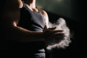 Close-up of unrecognizable strong man clapping hands with talc and preparing for workout at gym....