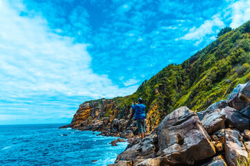 Monte Ulia in the city of San Sebastián, Basque Country. Visit the hidden cove of the city called Illurgita Senadia or Illurgita Senotia. A young man in a blue jacket in the cove taking a photo