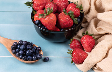 Juicy and fresh organic blueberries on a wooden spoon, and strawberries in a bowl.
Concept for healthy nutrition.
Close up view.
Tropical fruit  background.