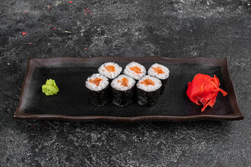 Maki Sushi Rolls with salmon on black stone on dark background. With ginger and wasabi. Sushi menu. Japanese food. Closeup of delicious japanese food with sushi roll. Horizontal photo