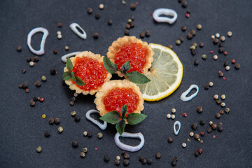 Red caviar in tartlets with  lemon and basil  on a black background.
