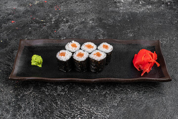 Maki Sushi Rolls with salmon on black stone on dark background. With ginger and wasabi. Sushi menu. Japanese food. Closeup of delicious japanese food with sushi roll. Horizontal photo
