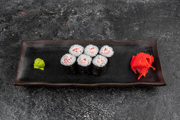 Sushi California Roll with crab meat, cucumber, masago, chopsticks on a gray plate, black background, side view