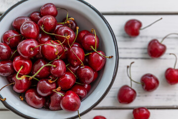 Scattered berries of ripe cherries on a light wooden background and in a bowl. Top view. Seasonal Vitamins.