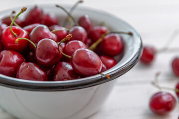 Scattered berries of ripe cherries on a light wooden background and in a bowl. Side view. Seasonal Vitamins.
