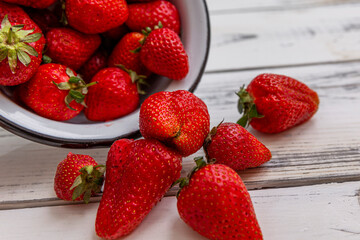 Berries of ripe red strawberries in a bowl on a light wooden background. Seasonal Vitamins. Close-up.