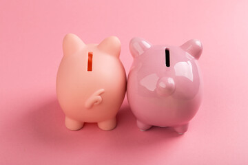 Two pink piggy banks on a pink background.