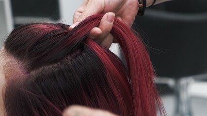 Professional hairdresser plaiting braids to red colored female hair