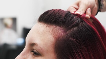 Professional hairdresser plaiting braids to red colored female hair