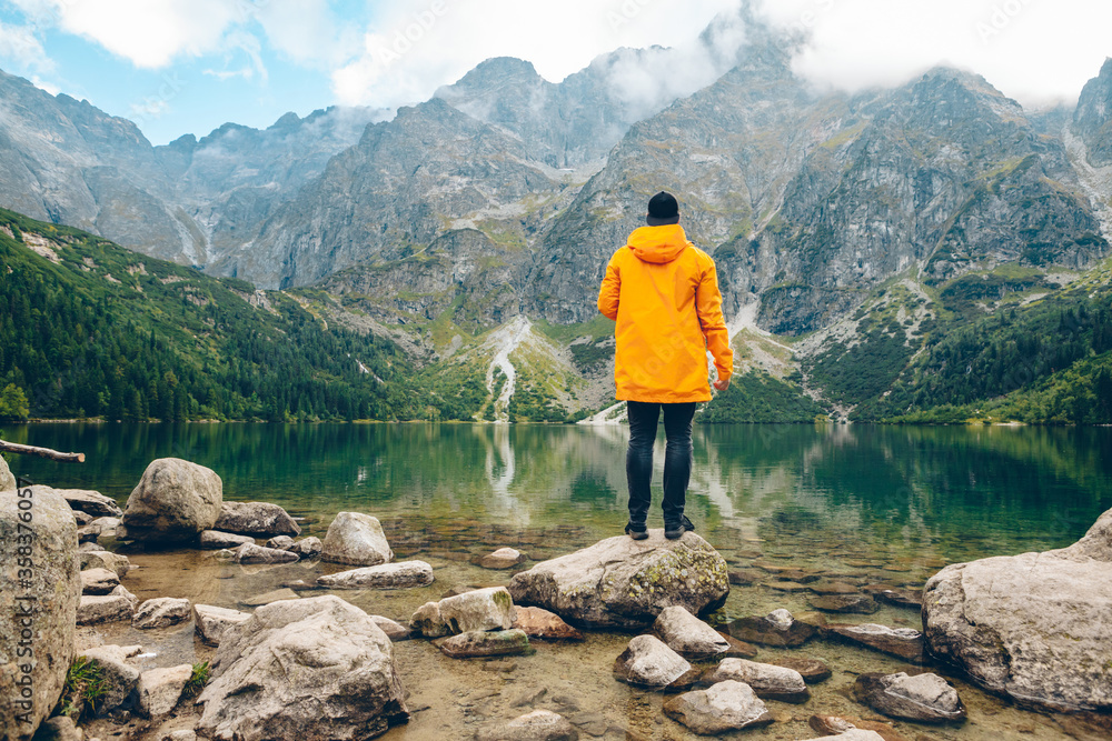 Wall mural man in yellow raincoat looking at lake in mountains